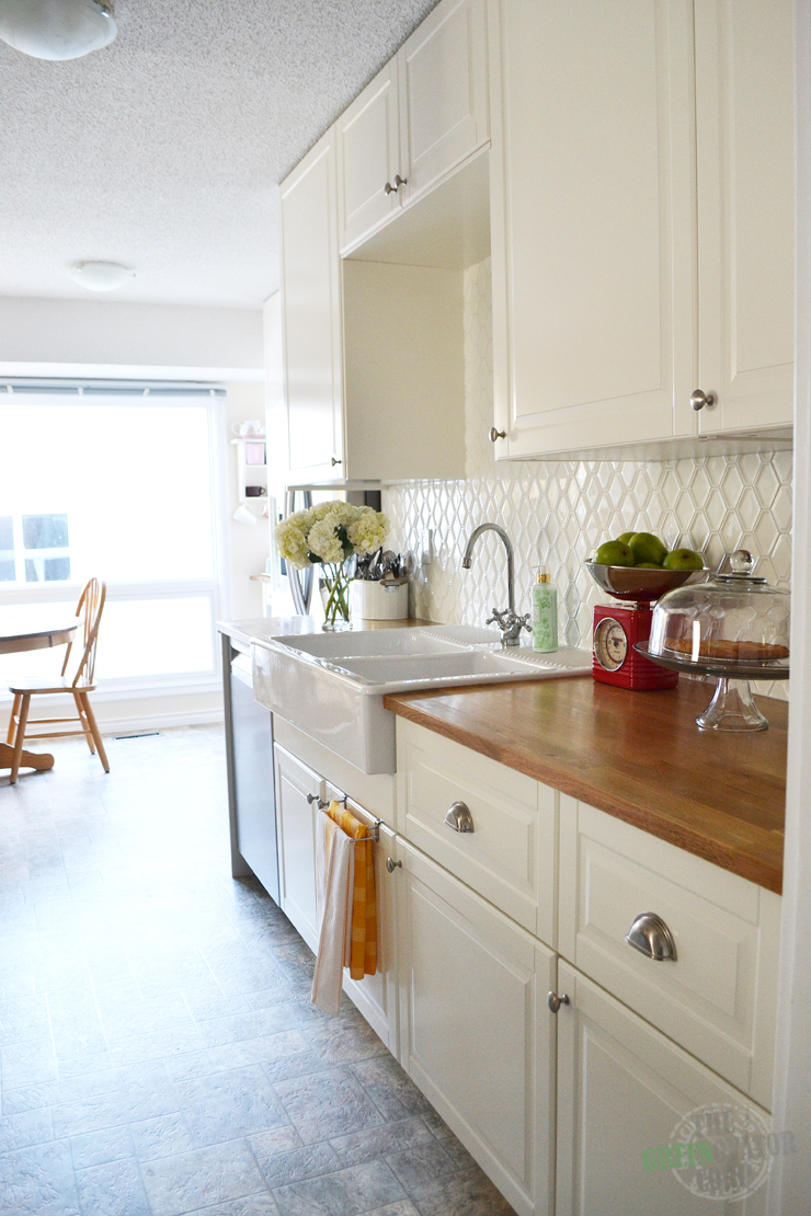 A bright white Ikea galley kitchen renovation with butcher block counters, hexagon tiles, stainless steel appliances.